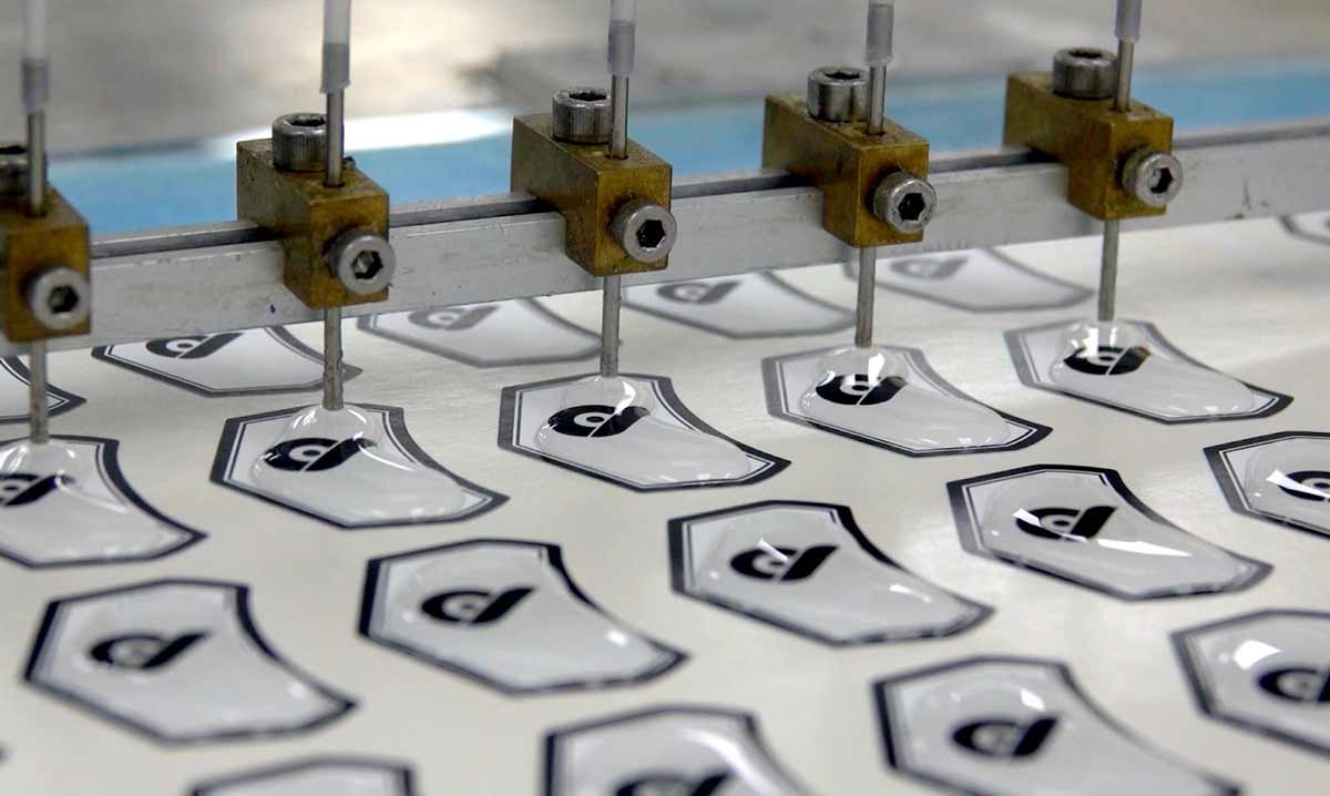 Domed emblem material being poured onto logos