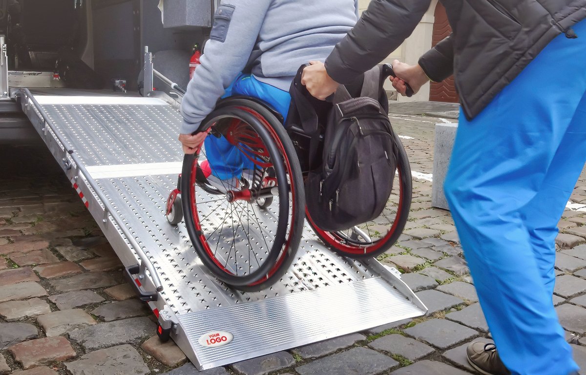 person in a wheelchair being assisted up a ramp