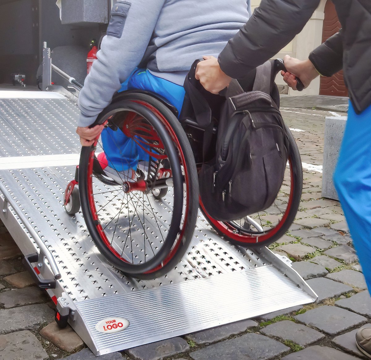person in a wheelchair being assisted up a ramp